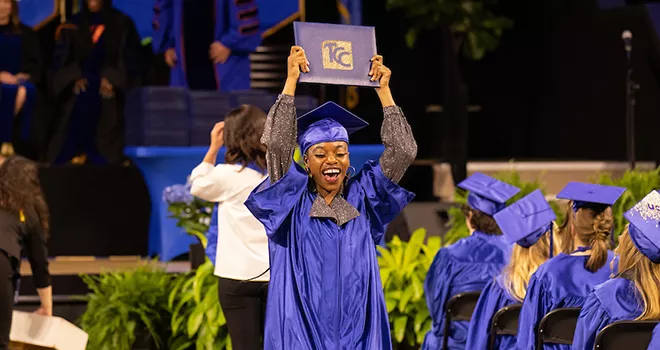 澳门线上博彩 Graduate in cap and gown hold diploma cover over her head.