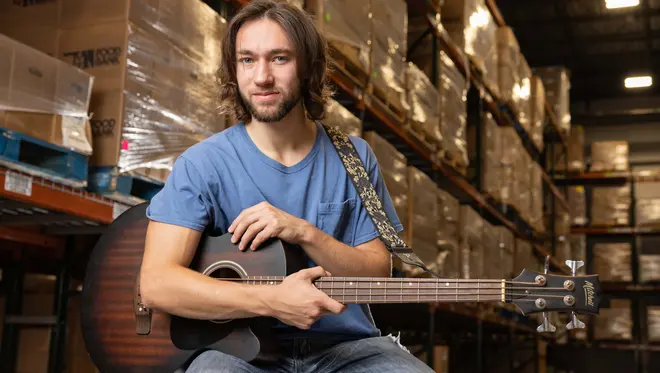 Christopher Capra holds a guitar with pallets of food behind him