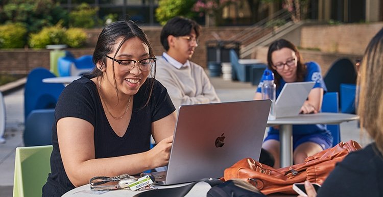 Young 澳门线上博彩 student works on her lap top at a table outside on the Southeast Campus.