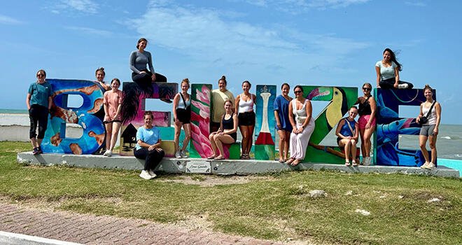 澳门线上博彩 early childhood students stand next to a sign spelling the word "Belize"